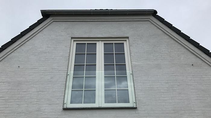 Hvidt hus med et stort vindue på taget, der viser en grå himmel i baggrunden.