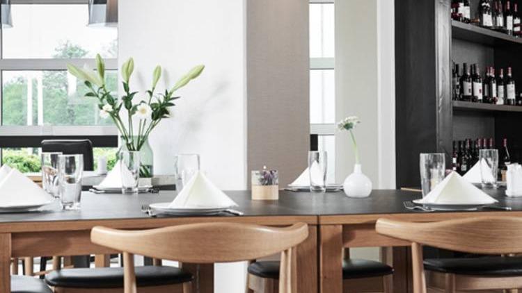 Moderne restaurantindretning med træbord, hvide servietter og blomster i vase. Baggrund med vinreol.