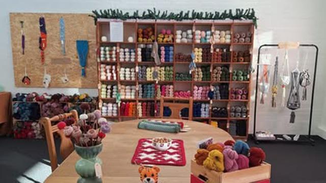 En hyggelig garnbutik med farverigt garn på hylderne, et rundt bord med dekorationer og strikketilbehør.