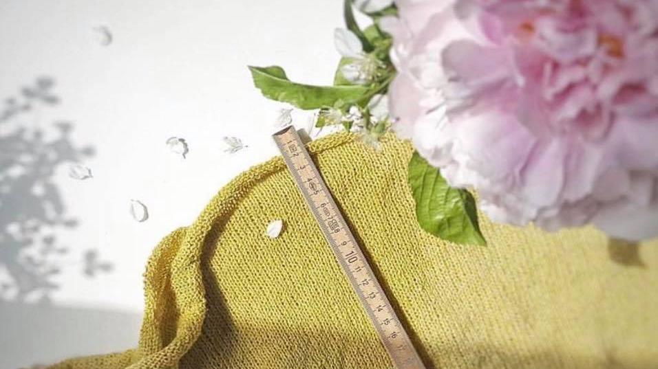 En gul klud med en lineal og en lyserød pæonblomst på en hvid overflade. Blomsterblade ligger spredt omkring.