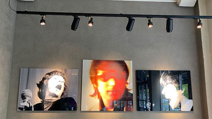 Tre farverige vægmalerier af berømte musikere hænger på en grå væg i en moderne café.