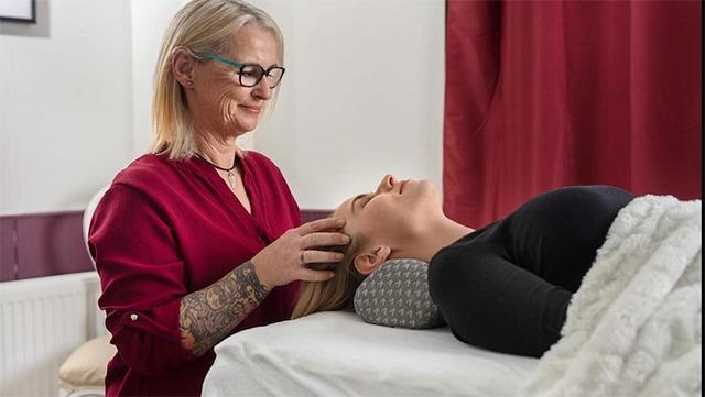En kvinde får en afslappende hovedbundsmassage af en terapeut i et lyst rum med røde gardiner.