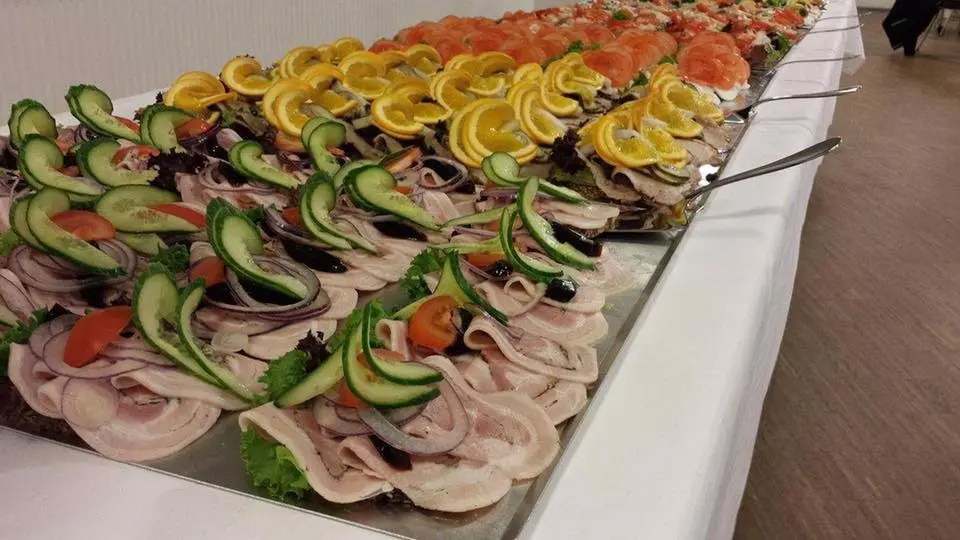 Frokostbord med smørrebrød toppet med skiver af pålæg, agurk, tomat og citrusfrugter.
