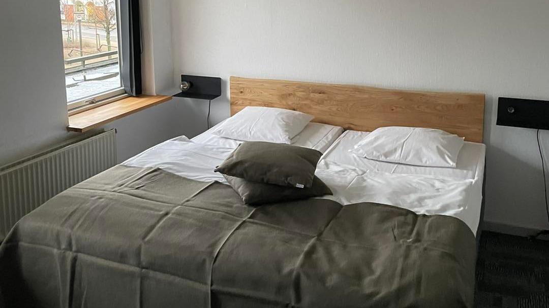 Et moderne soveværelse med en dobbeltseng, puder og en grøn plaid, beliggende ved et vindue.