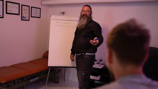 En mand med skæg står foran en tavle og præsenterer i et mødelokale.