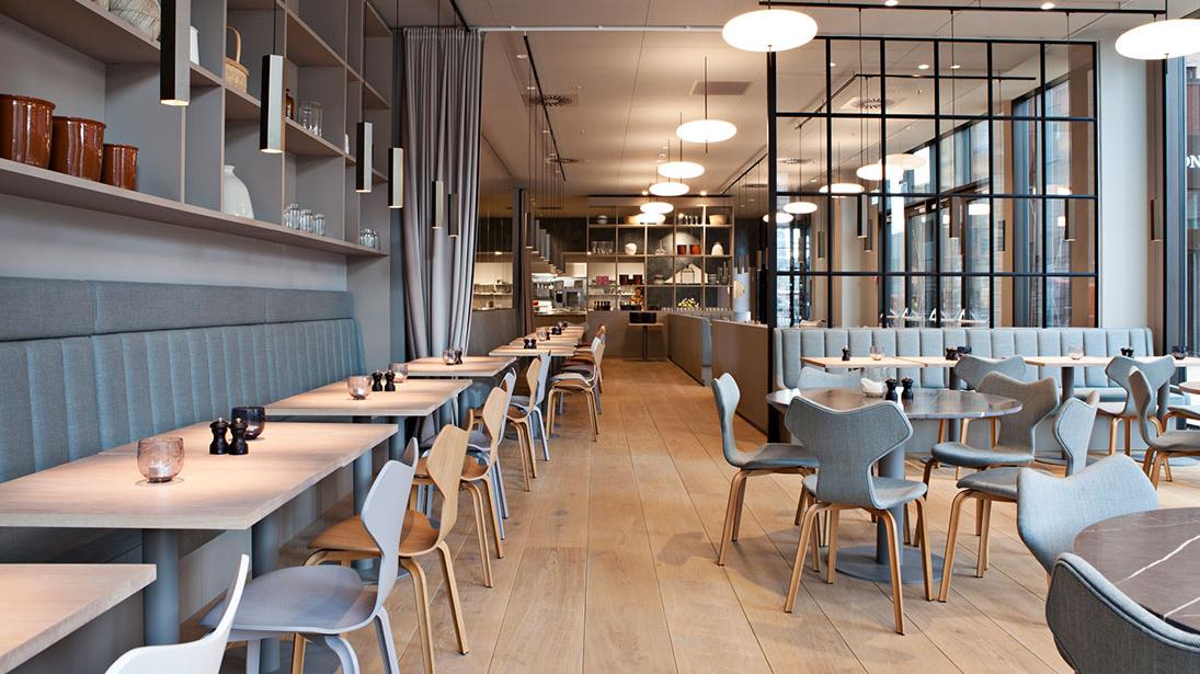 Moderne restaurantindretning med grå borde, stole og bløde belysningselementer.