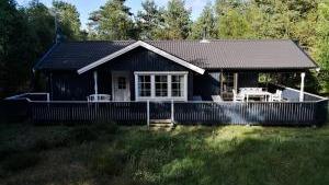 Et blåt hus med terrasse omgivet af træer og græs i et naturskønt område.