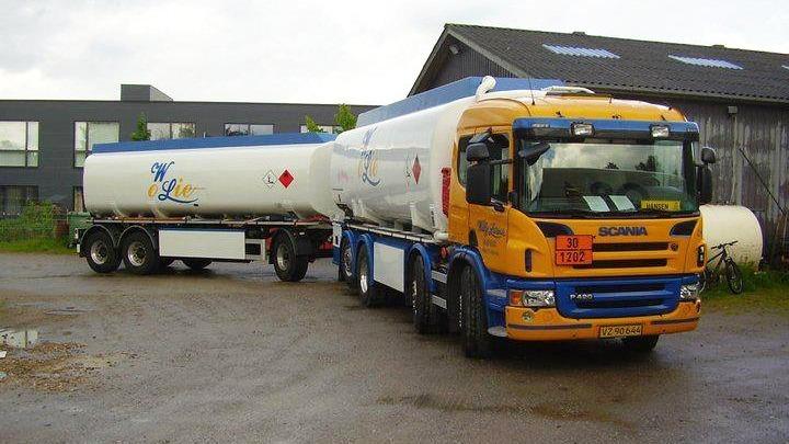 En lastbil med tankvogn, der transporterer kemikalier, parkeret på en grusvej ved en bygning.
