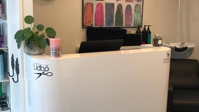 Modtagelsesområde i en frisørsalon med en hvid skranke og farverige malerier på væggen.