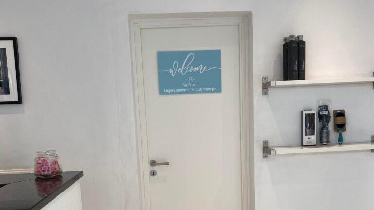 Dør til en skønhedssalon med skiltet "Velkommen" og hylder med skønhedsprodukter.