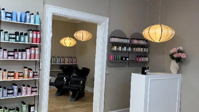 En frisørsalon med hylder fyldt med hårprodukter, to frisørstole og en reception med blomster.