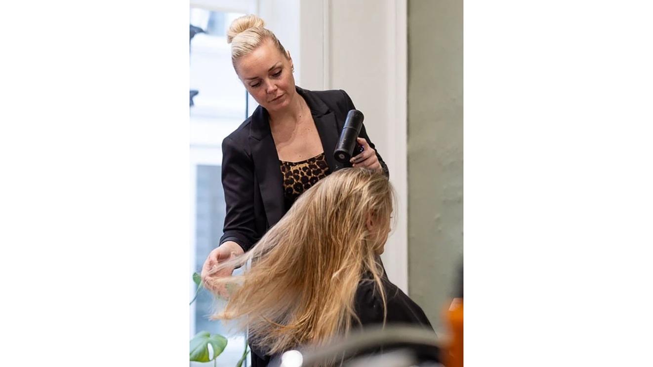 Frisør styler langt hår med en hårtørrer i en moderne salon.