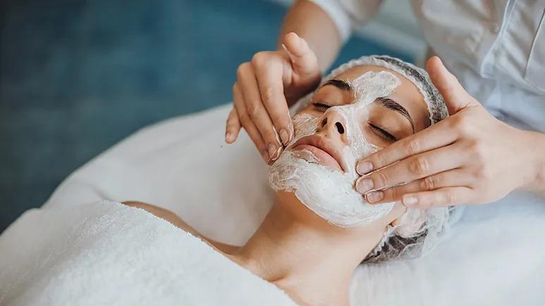 Kvinde får ansigtsbehandling med skummaske på en spa, mens en behandler masserer hendes ansigt.