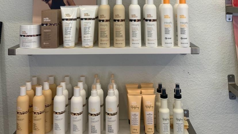 Hylder med forskellige hårprodukter i flasker og tuber, herunder shampoo, balsam og stylingprodukter.