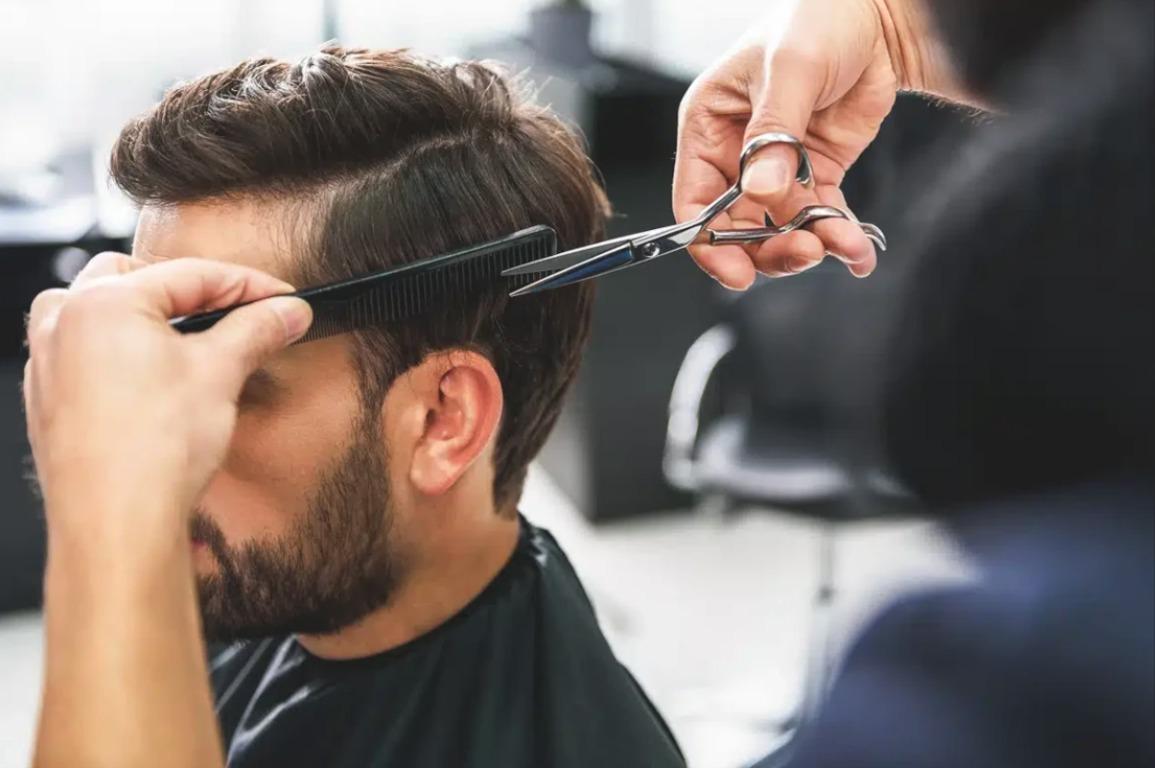 En frisør klipper håret på en mand med en kam og saks i en moderne frisørsalon.