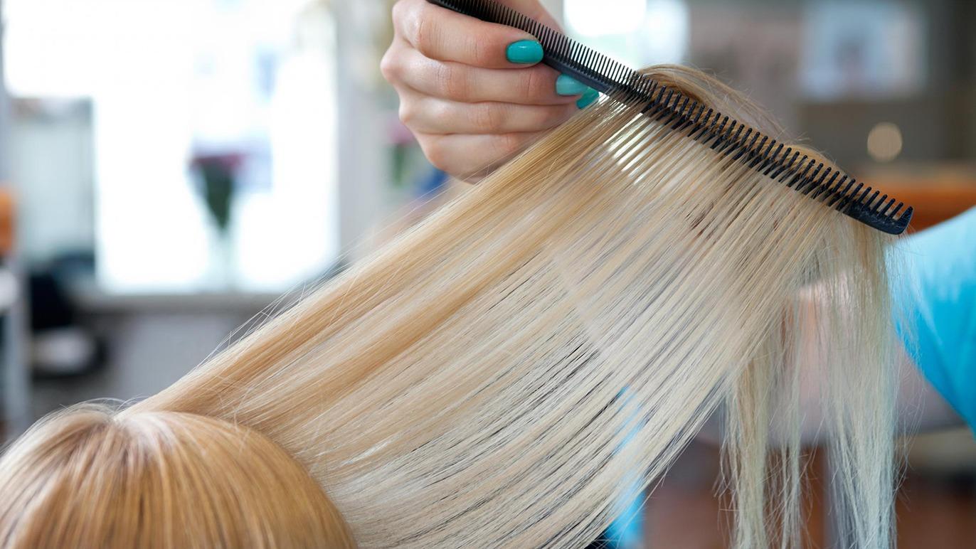 En frisør kæmmer blont hår med en sort kam i en salon.