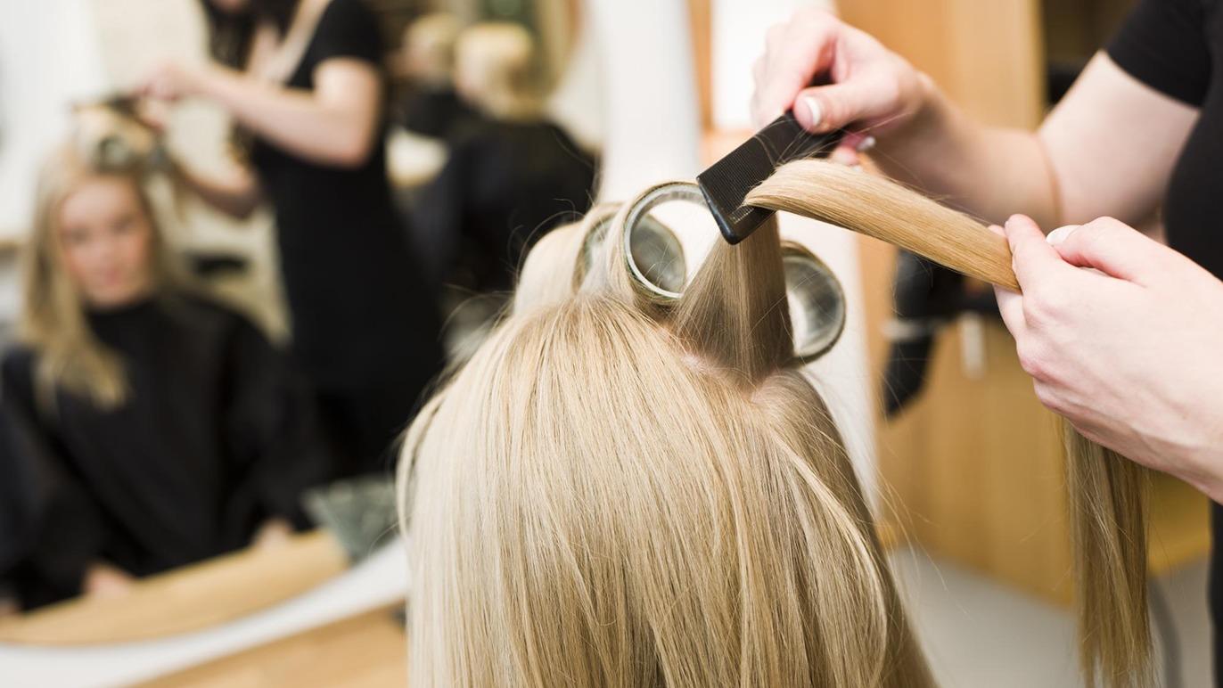 En frisør styler langt, lyst hår med en rundbørste i en moderne frisørsalon.