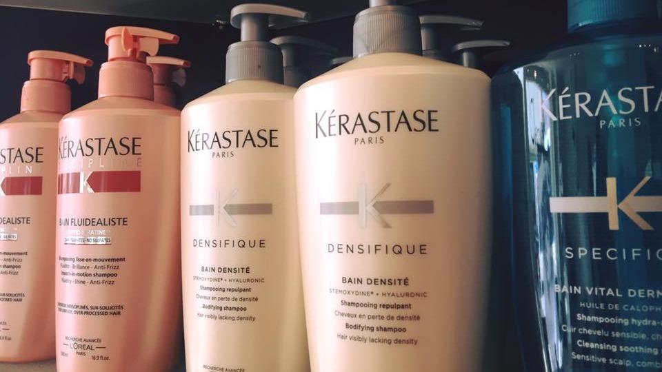 Flasker med Kérastase hårplejeprodukter i forskellige farver og størrelser på en hylde.