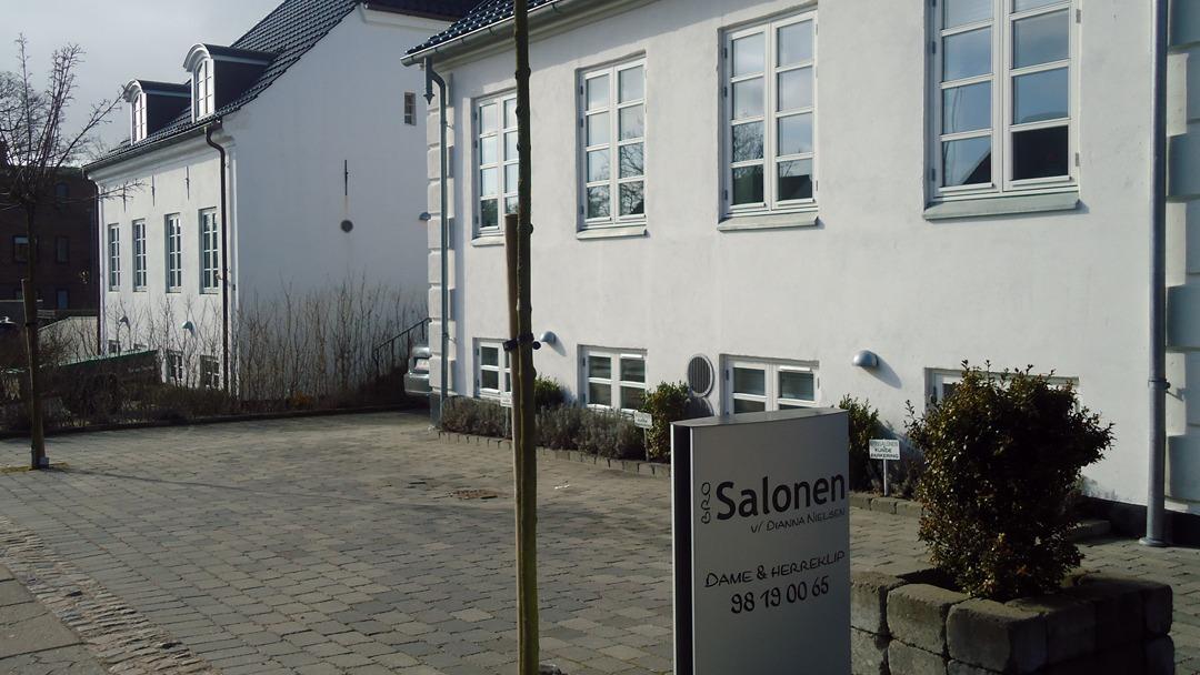 En hvid bygning med vinduer og en skilt, der viser "Salonen", på en brostensbelagt gård.