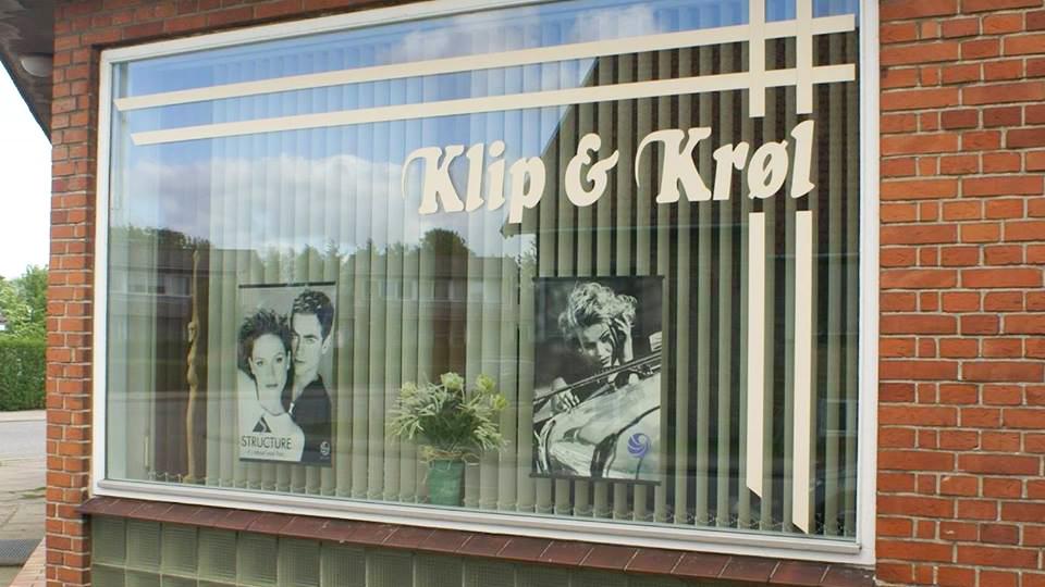 Frisørsalonens vindue med navnet "Klip & Krøl" og billeder af frisurer.