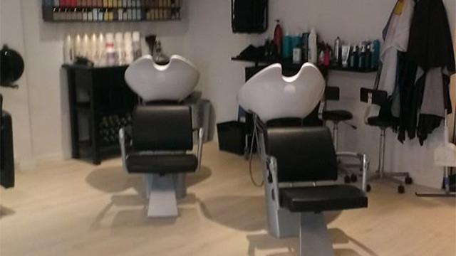 To stole i en frisørsalon med sort læderbetræk og produkter på hylderne i baggrunden.