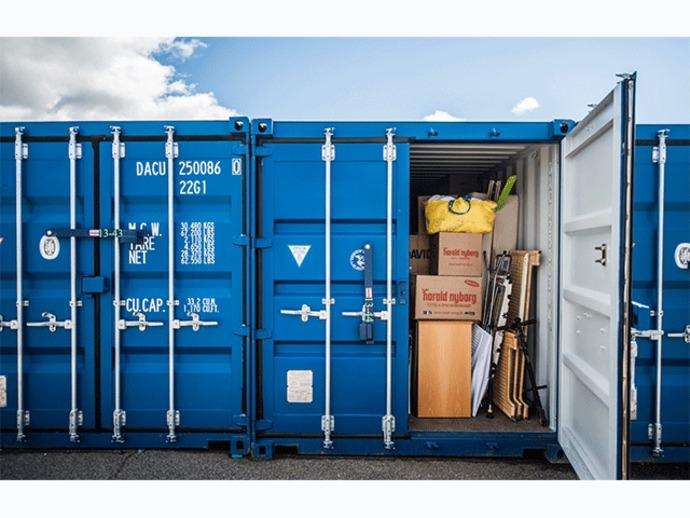 Blå container med åbne døre, der viser kasser, værktøj og en gul pose indeni.