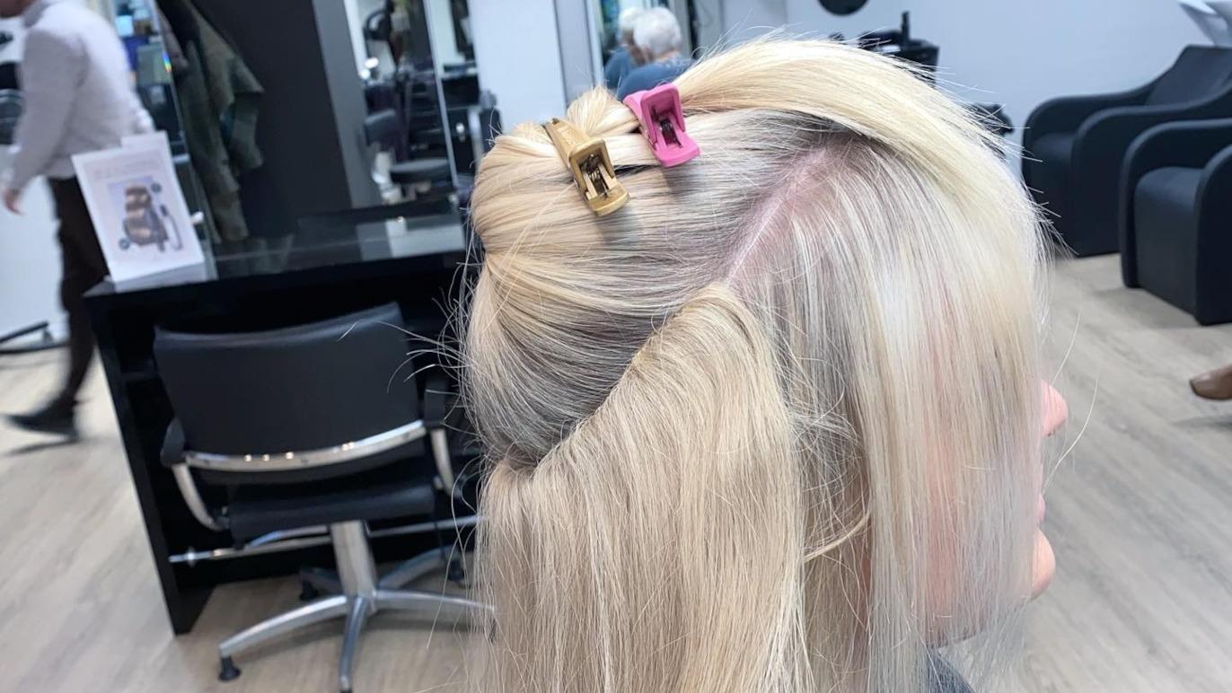 En frisørklient med lyst hår, der er delt op og fastgjort med hårnåle i en moderne salon.