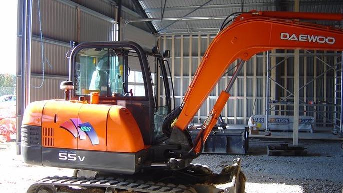 En orange gravemaskine af mærket Daewoo står i en bygning under konstruktion.