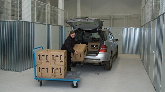 En person læsser kasser fra en bil ind i et opbevaringsrum med metalvægge.