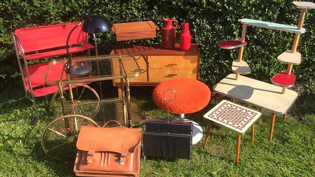 En samling af retro møbler og tilbehør, herunder stole, borde, lamper og opbevaringskasser i forskellige farver.
