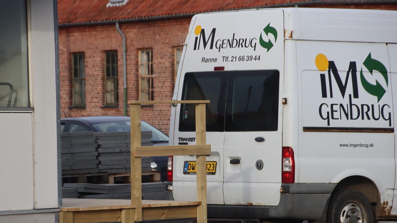 En hvid varevogn med teksten "iM Gendrug" parkeret ved en bygning med mursten.