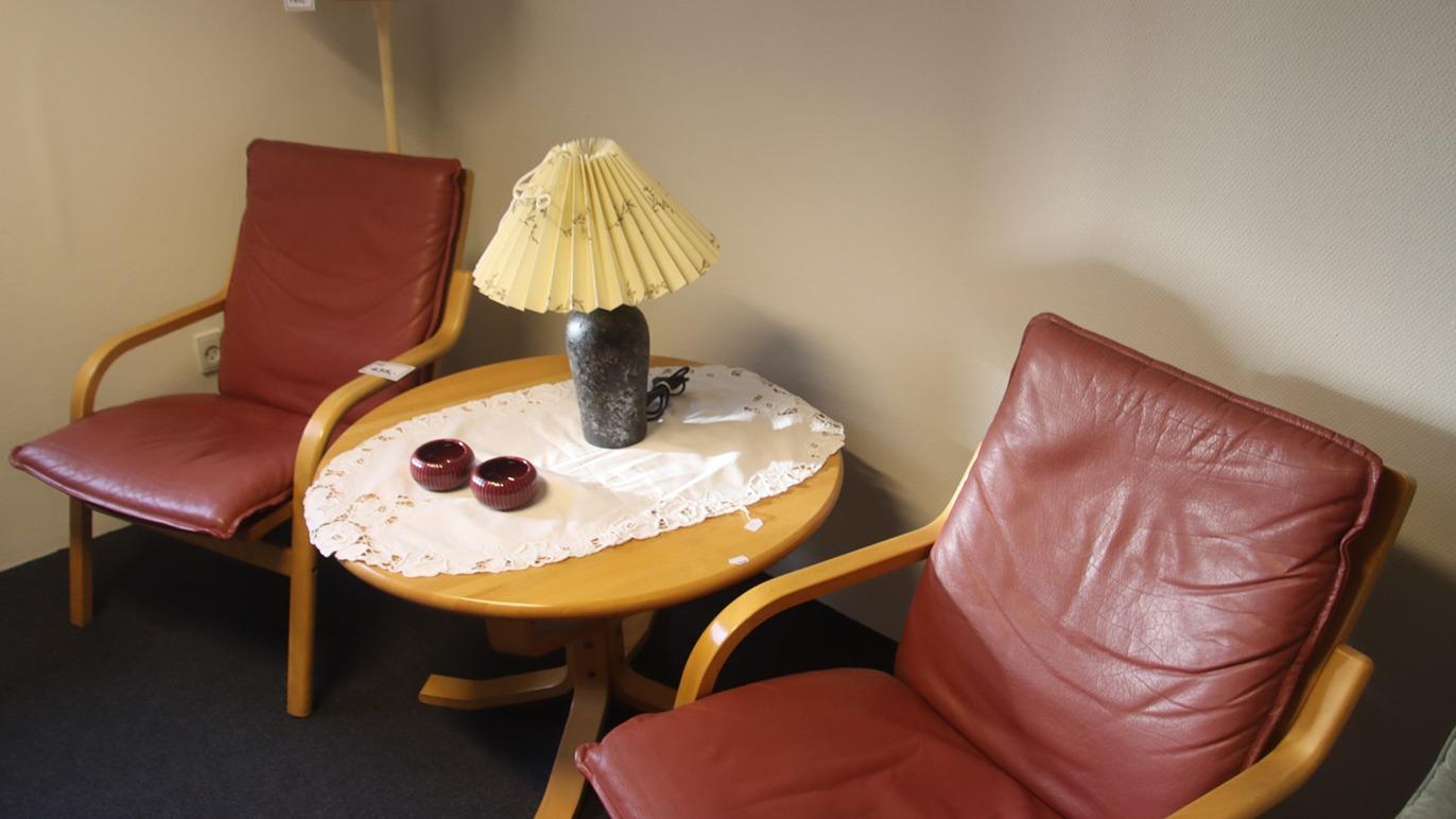 To sene læderstole ved et rundt bord med en lampe og to skåle på en hvid dug.