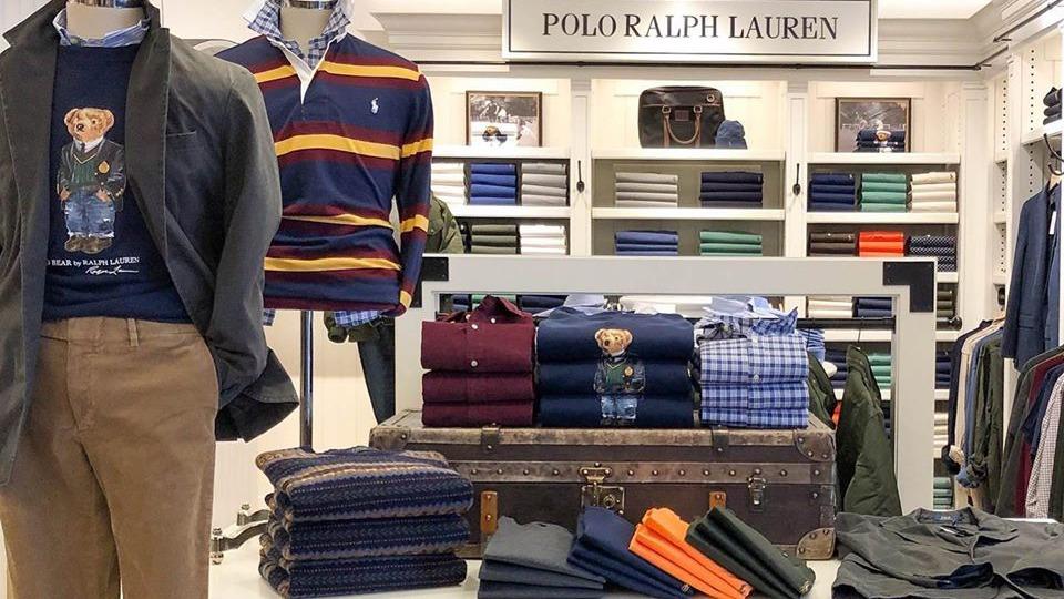 Butiksvindue med Polo Ralph Lauren tøj, herunder skjorter, bukser og en kuffert som dekoration.