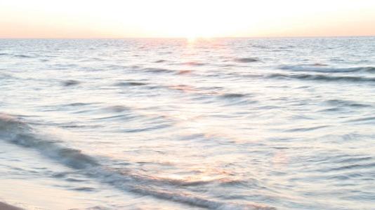 Solnedgang over havet med bløde bølger, der skvulper mod stranden i det gyldne lys.