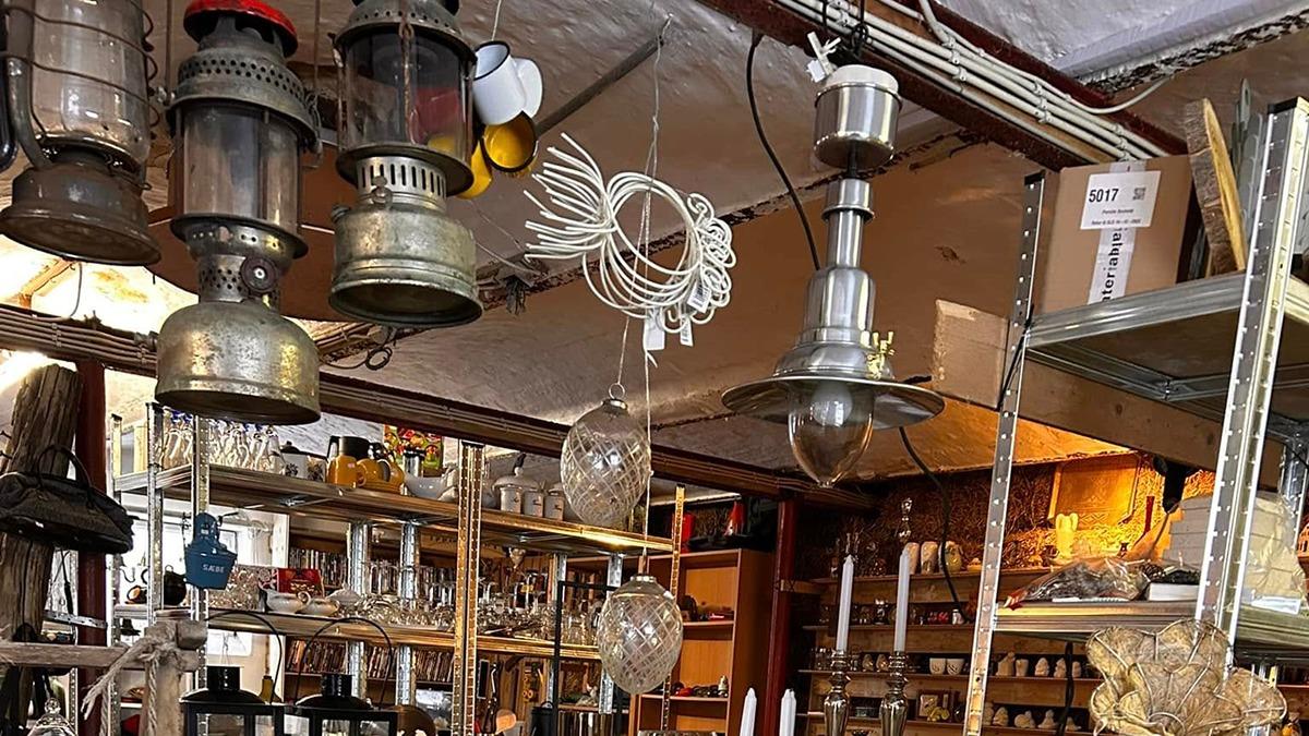 En butik med forskellige lamper og glasvarer hængende fra loftet, samt hylder fyldt med glas og køkkenudstyr.