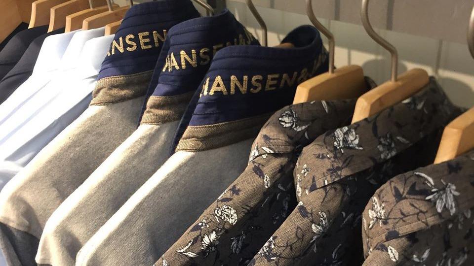 Skjorter hængende på bøjler i en butik, med forskellige farver og mønstre, herunder blomsterdesign.