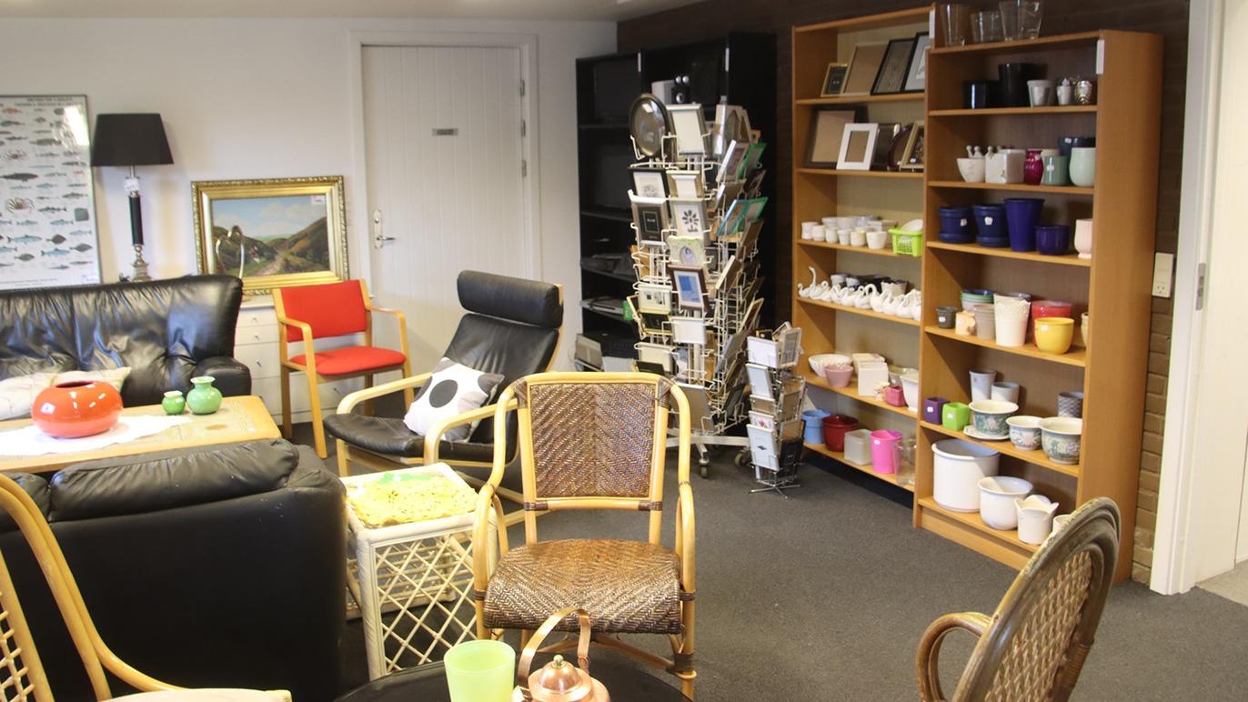 Stue med forskellige møbler, herunder stole, sofa og reol med farverige kopper og billeder.