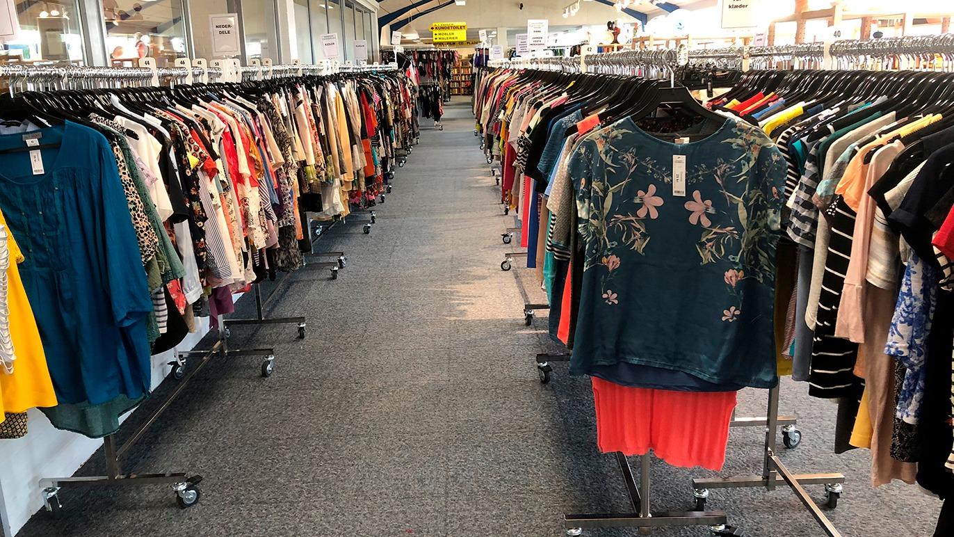 En lang række tøj på bøjler i en butik, med farverige bluser og kjoler på begge sider.