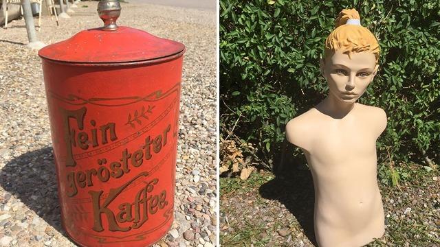 Rød kaffeboks med tekst og en mannequin uden tøj med blond hår, stående i en have.