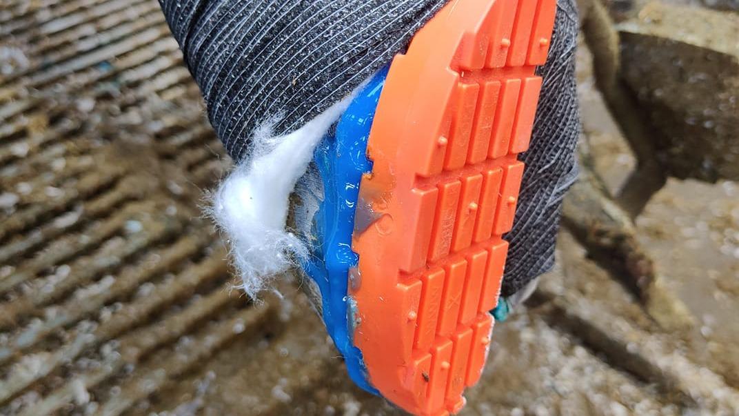 En nærbillede af en sko med orange sål og blå detaljer, der har fastgjort noget hvidt materiale.