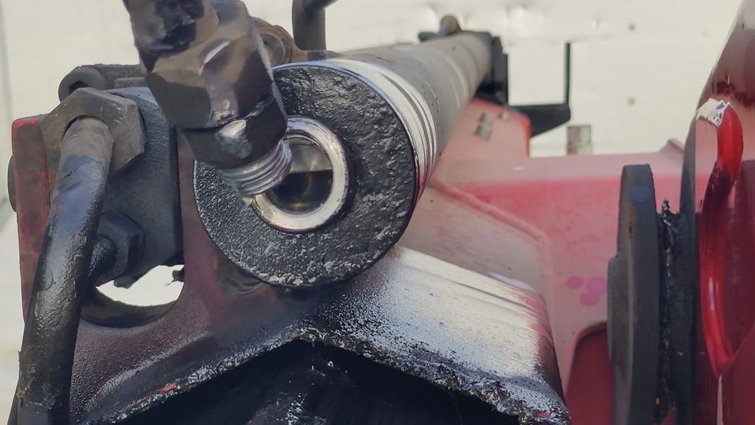 Nærbillede af en hydraulisk cylinder med olie og metaldele på en maskine.