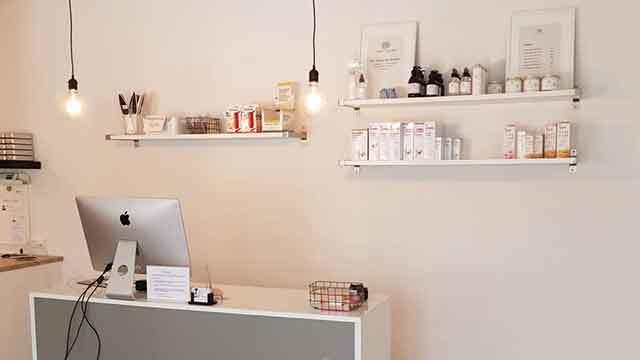 Moderne reception med hylder fyldt med skønhedsprodukter og en computer på bordet.
