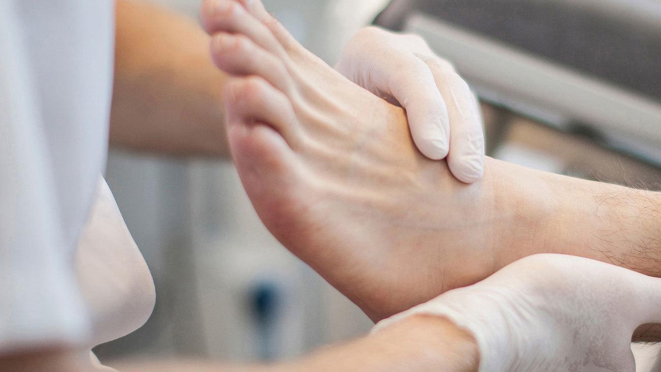En person får fodbehandling med en behandler, der undersøger foden med handsker på.