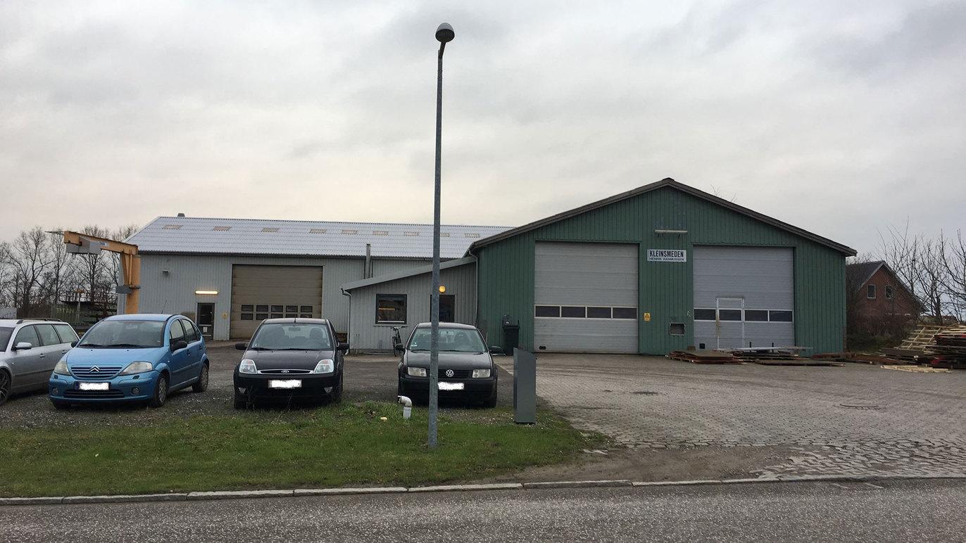 En grøn bygning med garageporte og flere biler parkeret foran på en grå dag.