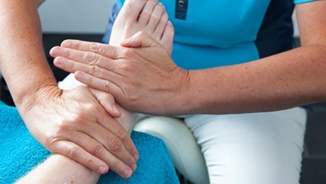 En behandler udfører fodmassage på en patient, der sidder på en stol med en blå håndklæde.