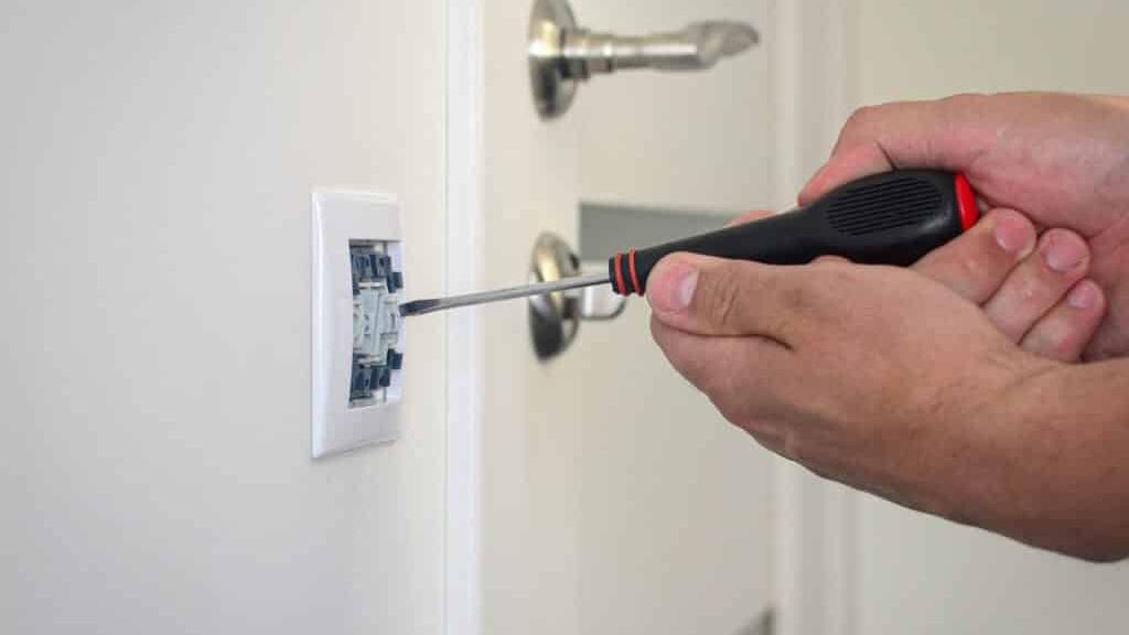 En hånd, der bruger en skruetrækker til at installere en elektrisk stikkontakt på en væg.