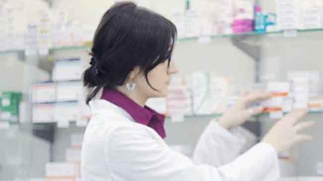 En farmaceut i hvid kittel står ved en hylde med medicin i et apotek.