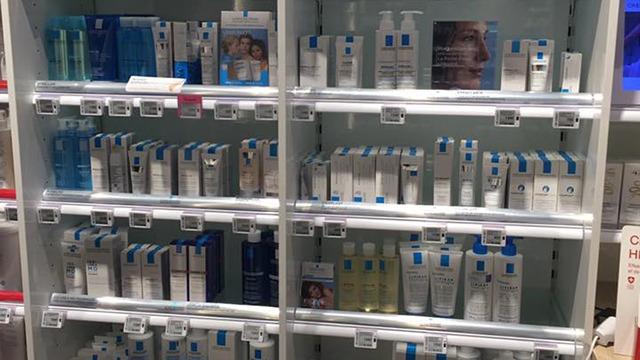 Hylder med forskellige hudplejeprodukter i en butik, herunder cremer, rensemidler og serum.