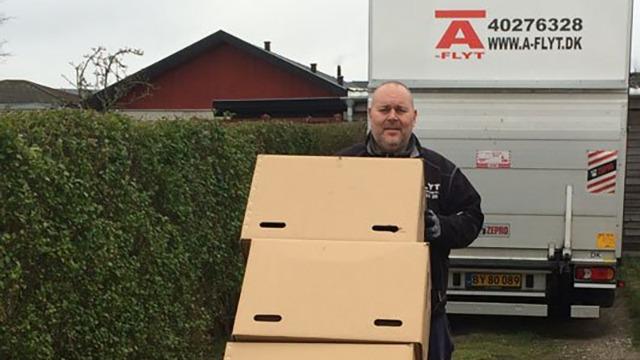 En mand står foran en flyttebil og holder to papkasser i hænderne.