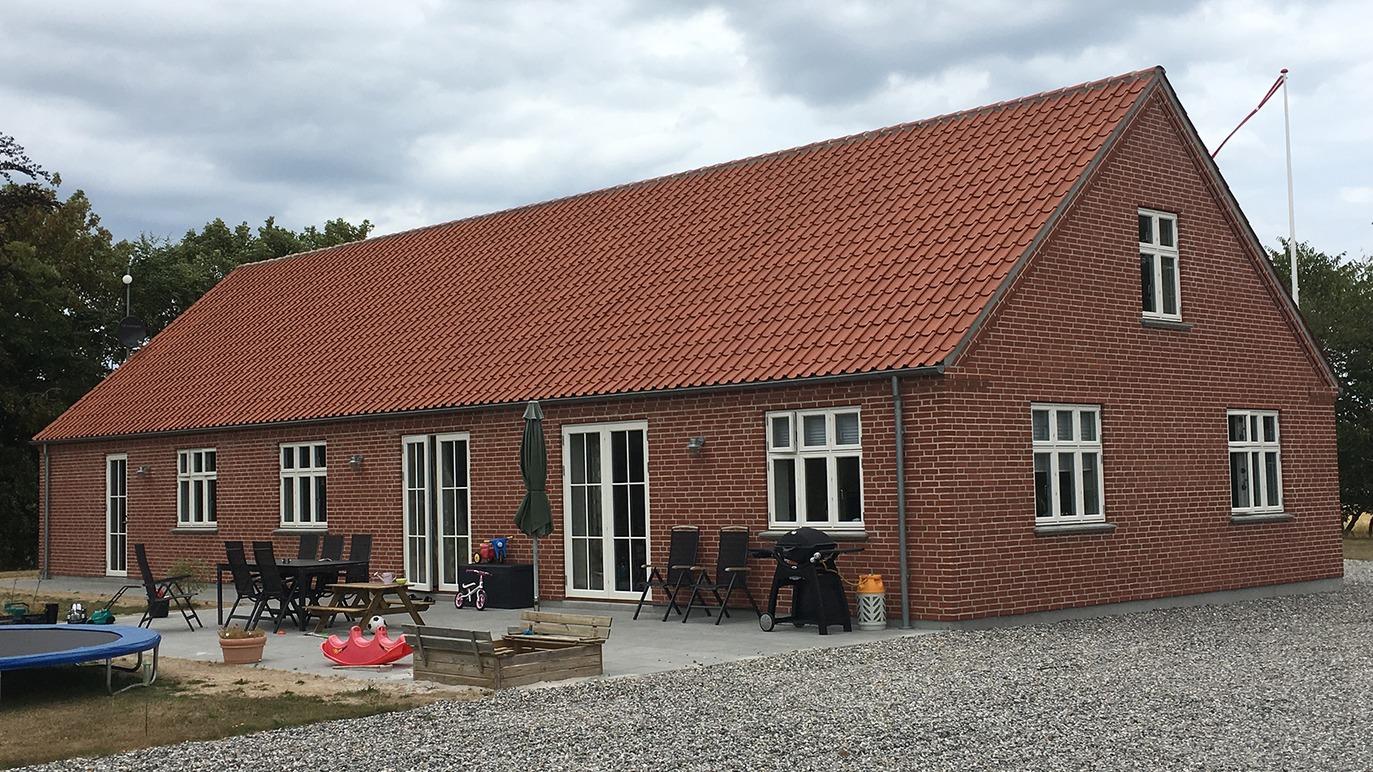 Et stort murstenshus med rødt tag, terrasse og havemøbler i en grusbelagt have.